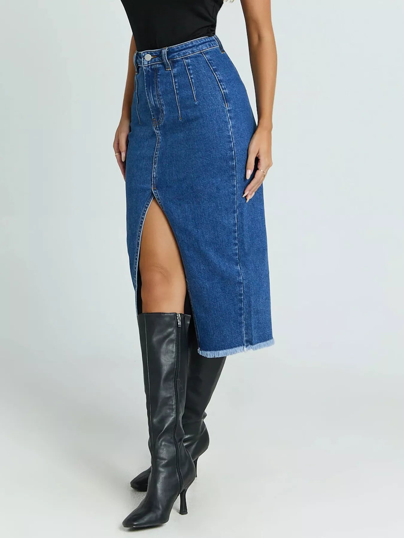 Person wearing a blue denim skirt with a high slit and black knee-high boots on a white background