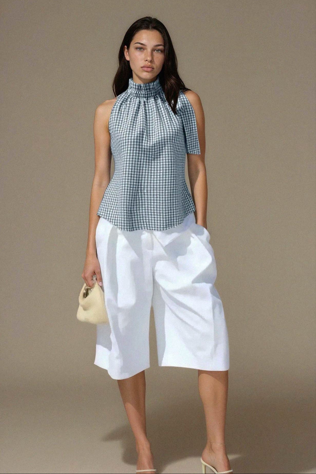 Woman wearing a checkered top and white pants against a brown background
