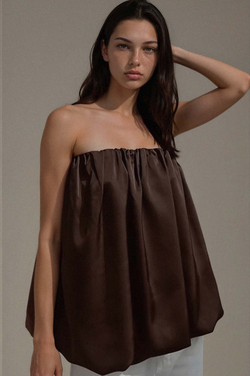 Woman wearing a brown strapless top against a beige background