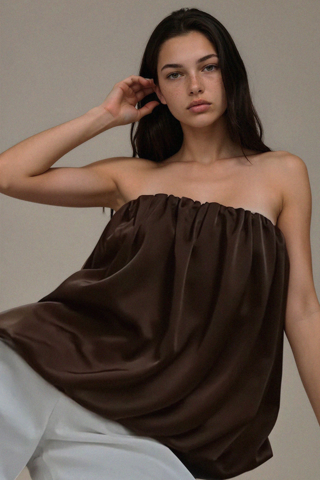 Woman wearing a brown strapless top and white pants against a neutral background