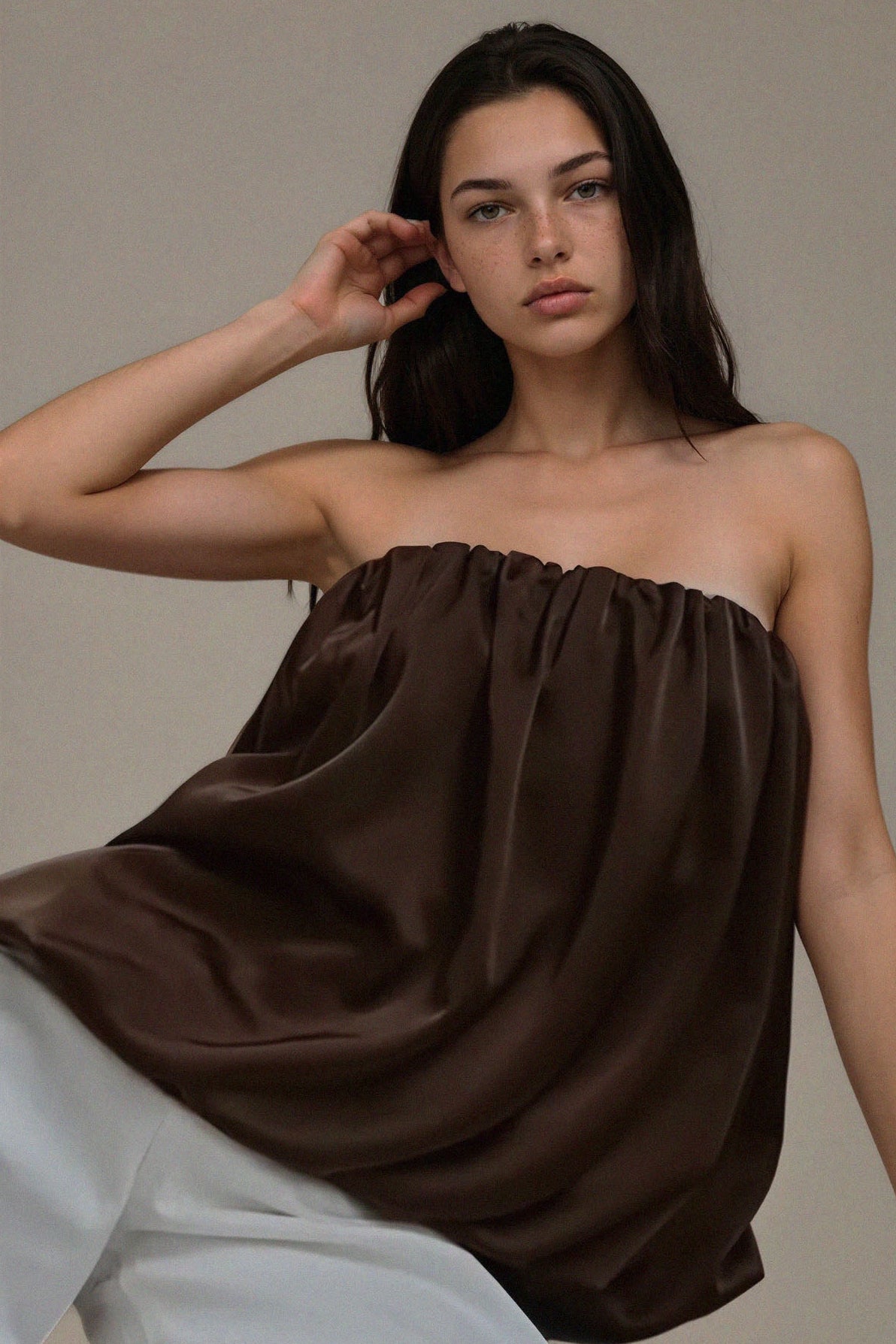 Woman wearing a brown strapless top and white pants against a neutral background