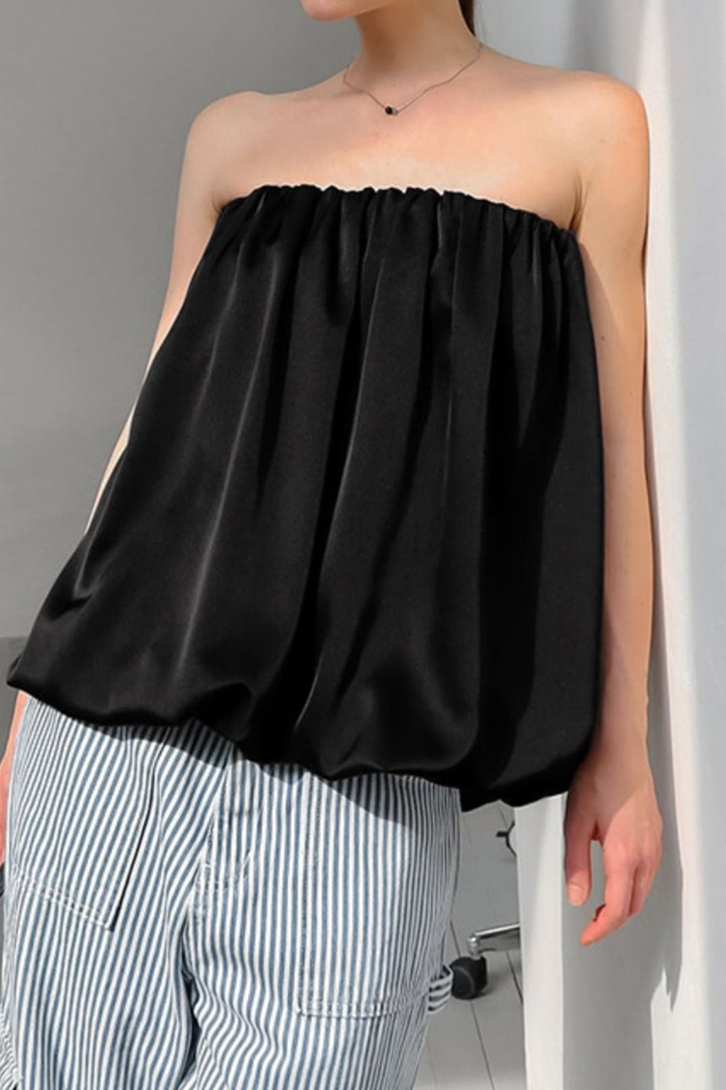 Person wearing a black strapless top and striped pants against a gray background