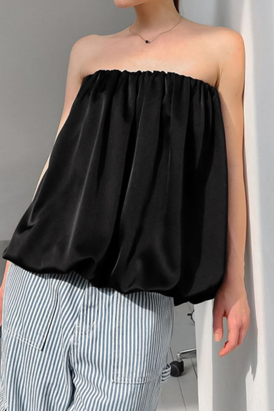 Person wearing a black strapless top and striped pants against a gray background