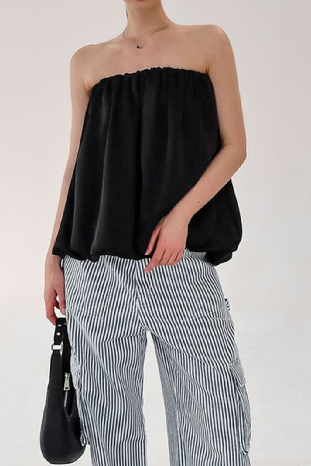 Person wearing a black strapless top and striped pants with a white background