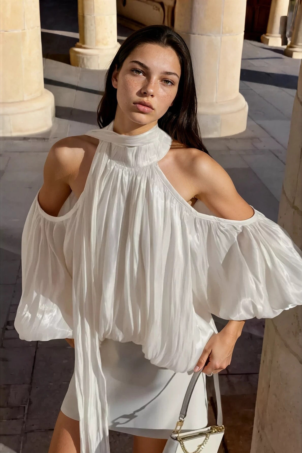 Woman wearing a white off-shoulder dress with long sleeves in an outdoor setting.