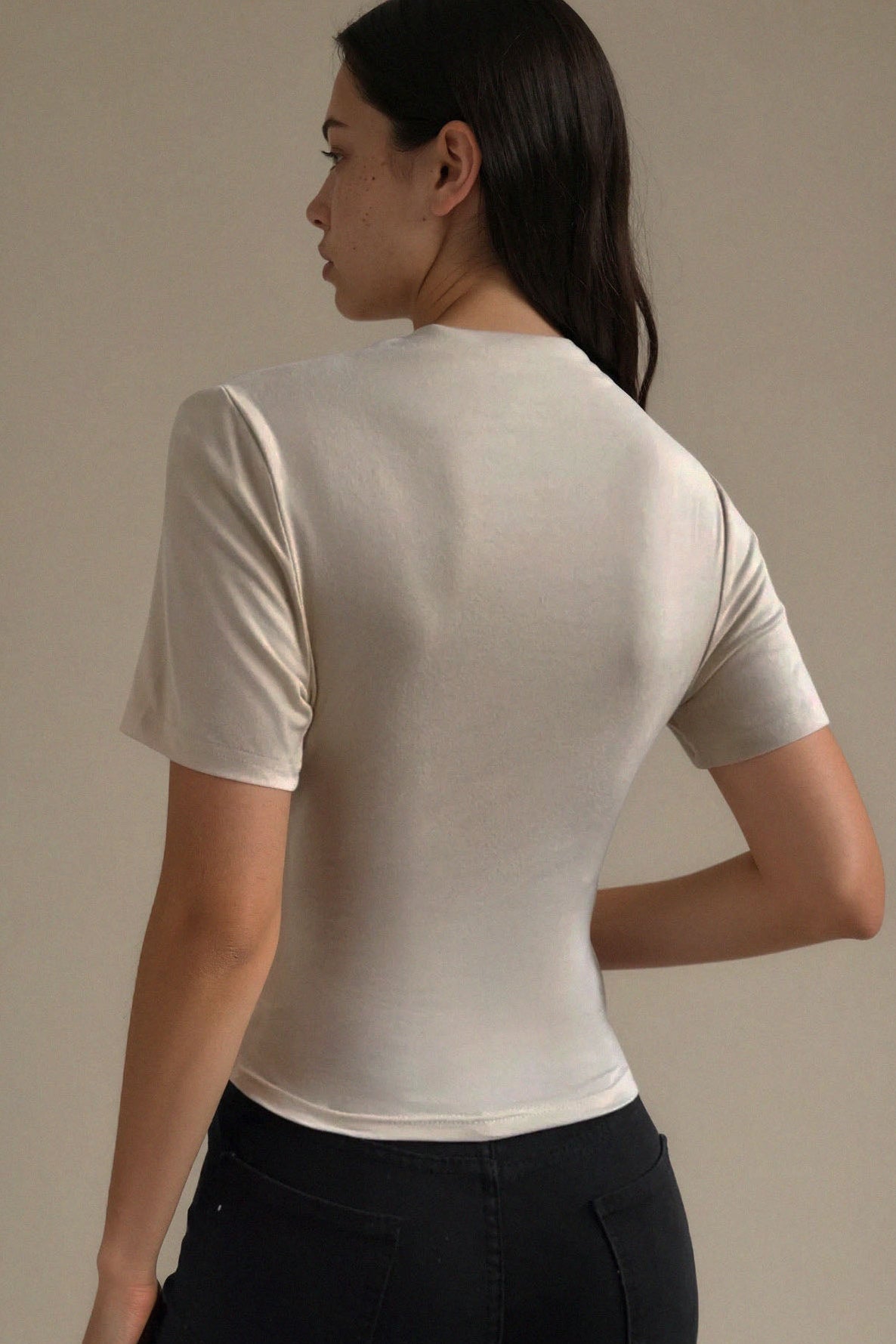 Woman wearing a beige short-sleeve top and black pants against a neutral background