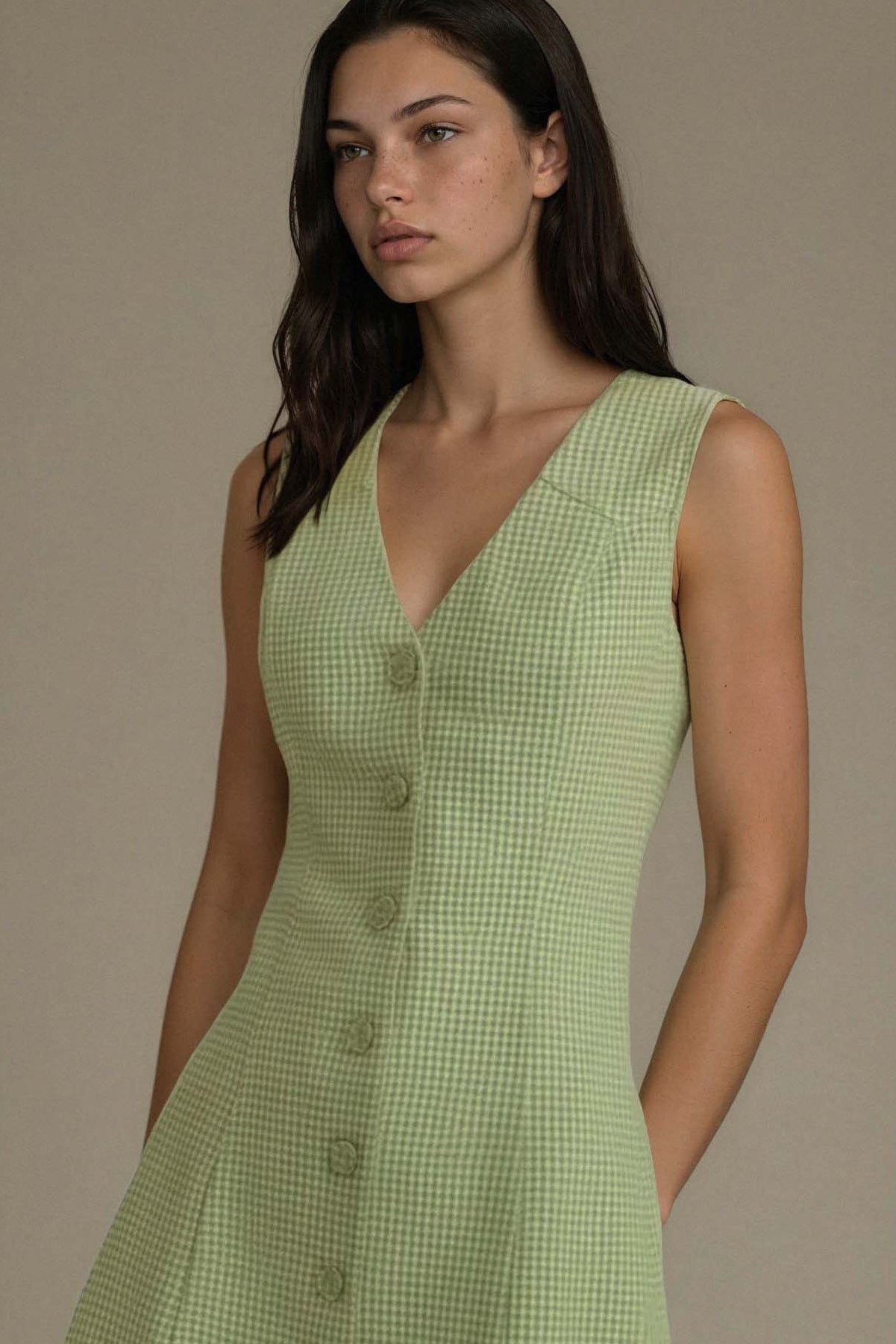 Woman wearing a green checkered dress against a beige background