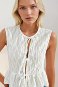 Woman wearing a white sleeveless top with lace details and blue jeans on a plain background