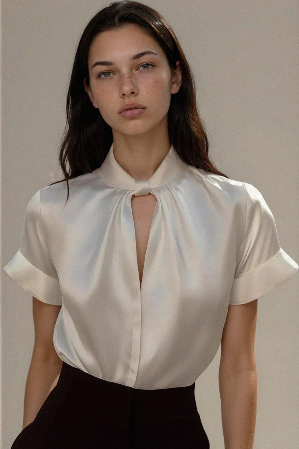 Woman wearing a white blouse with a keyhole neckline against a neutral background