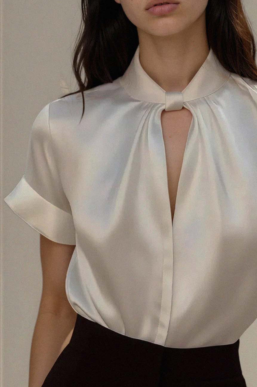 Woman wearing a white blouse with a keyhole neckline against a neutral background