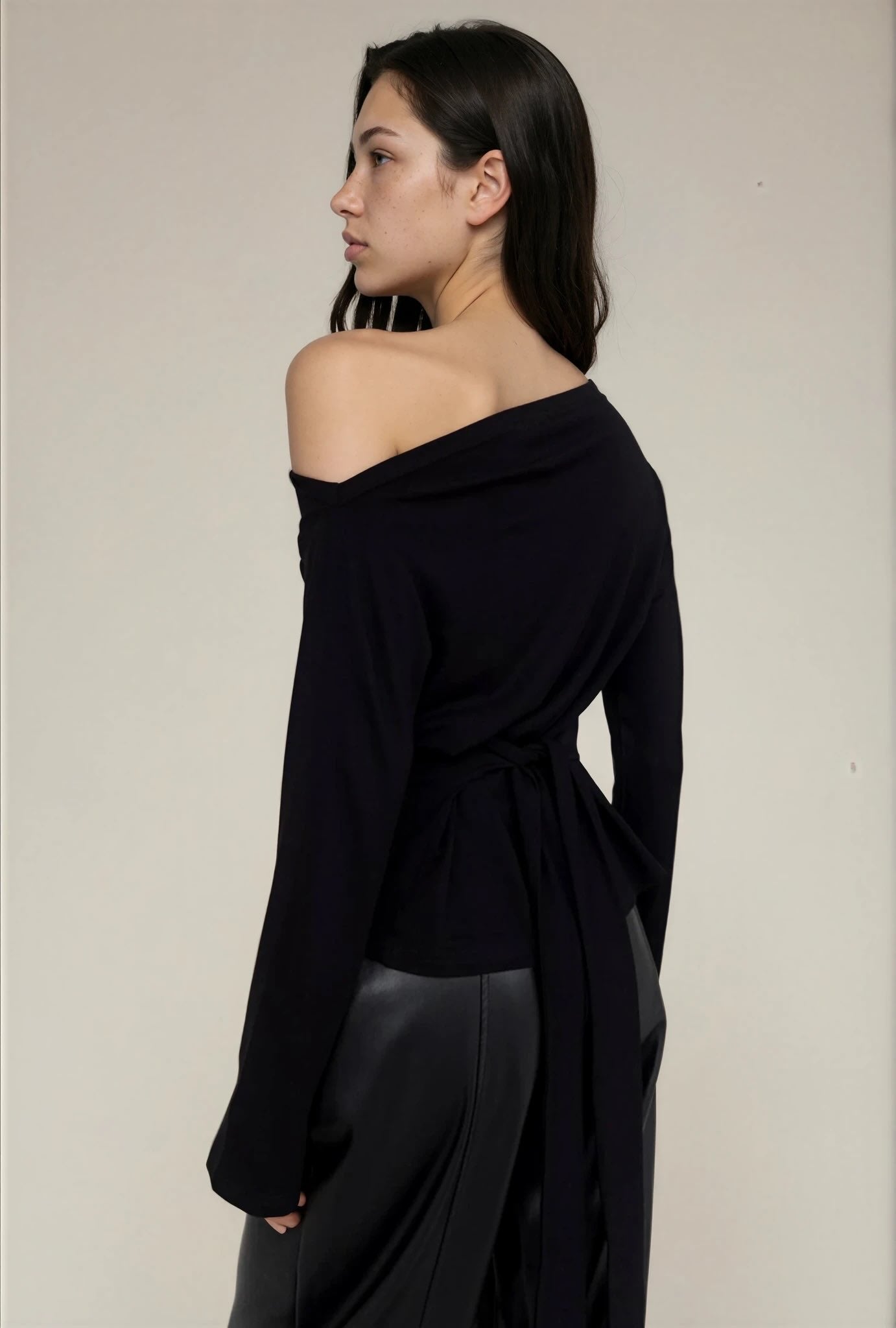 Woman wearing a black off-shoulder top and dark pants against a plain background