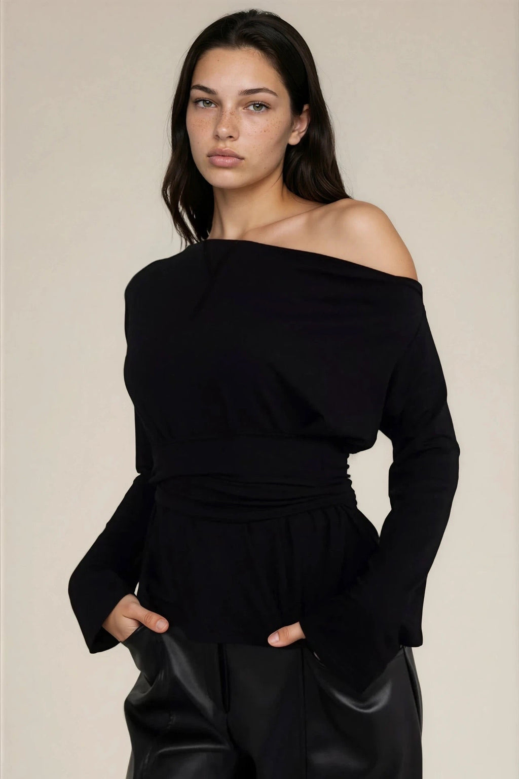 Woman wearing a black off-shoulder top and black pants against a beige background