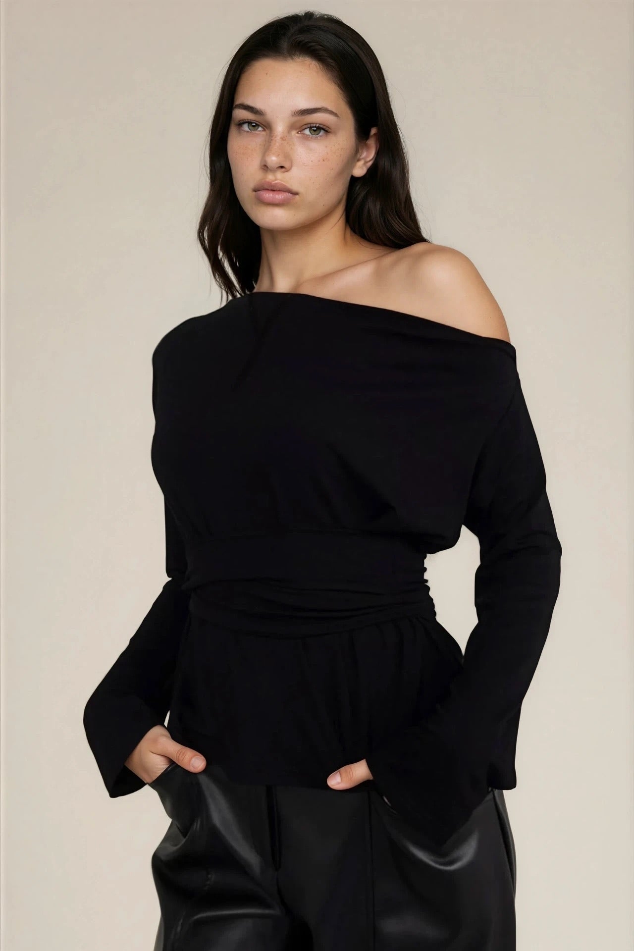 Woman wearing a black off-shoulder top and black pants against a beige background