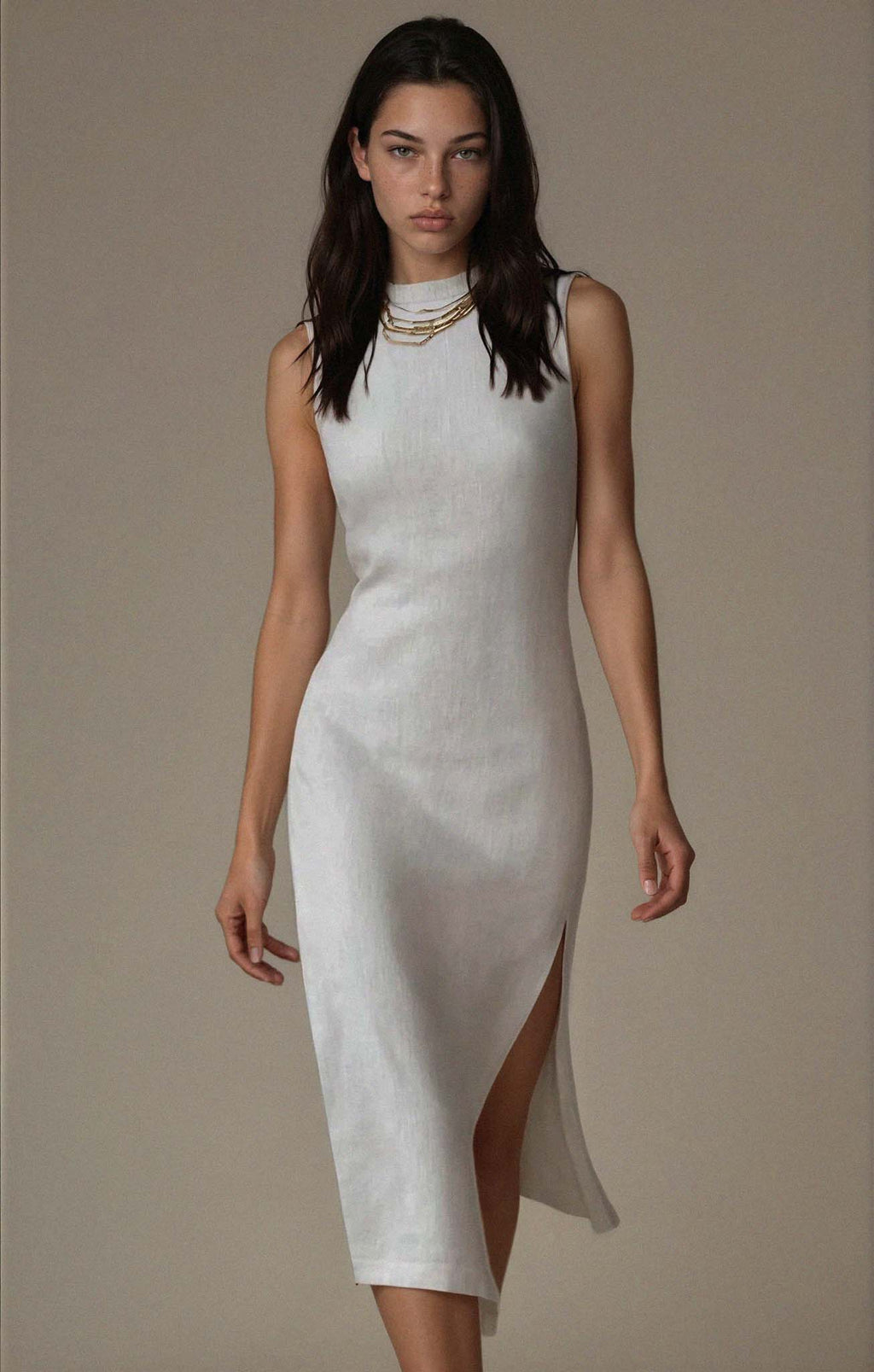 Woman wearing a white dress with a high slit on a plain background