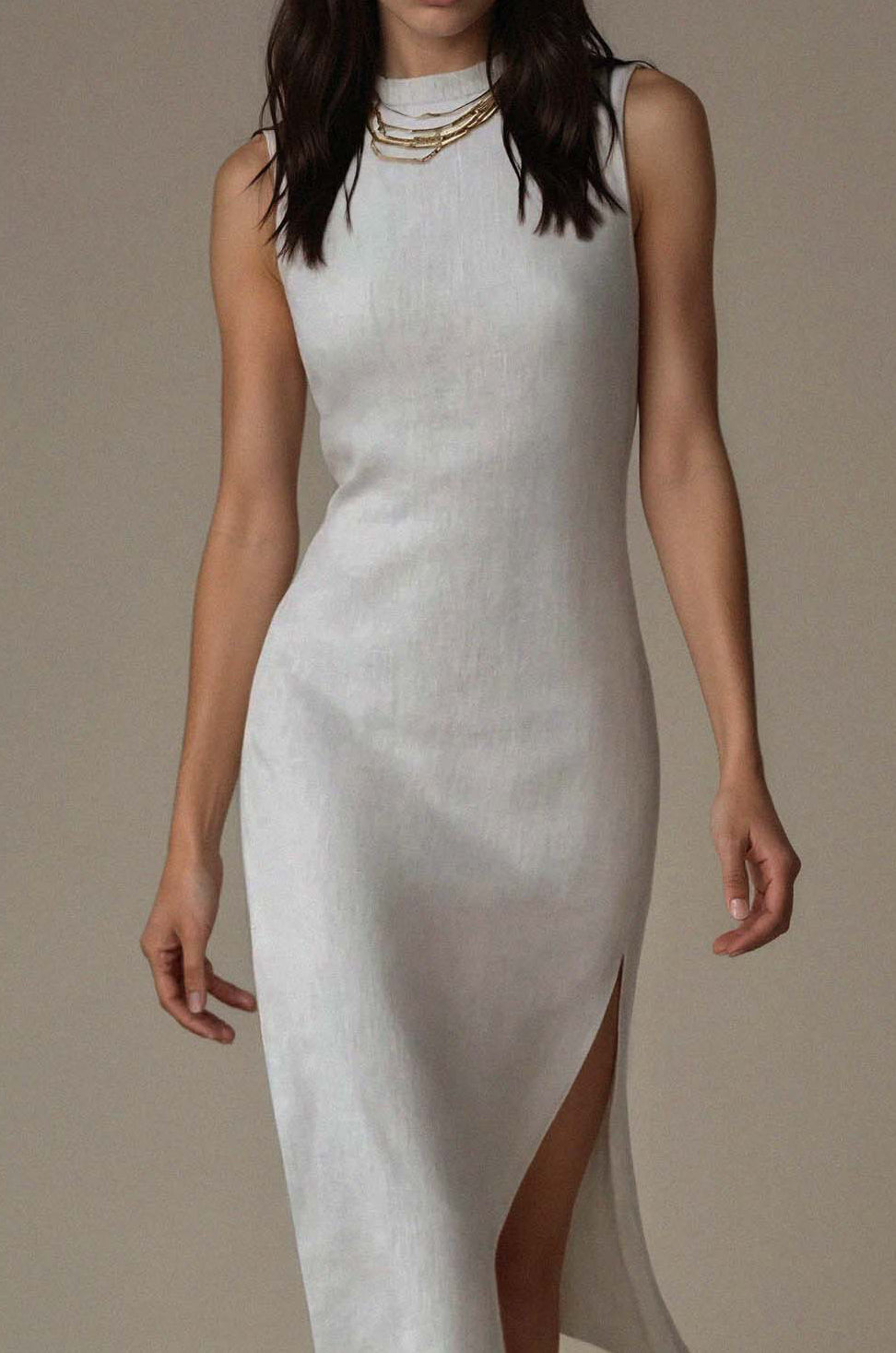 Woman wearing a white dress with a high slit on a plain background