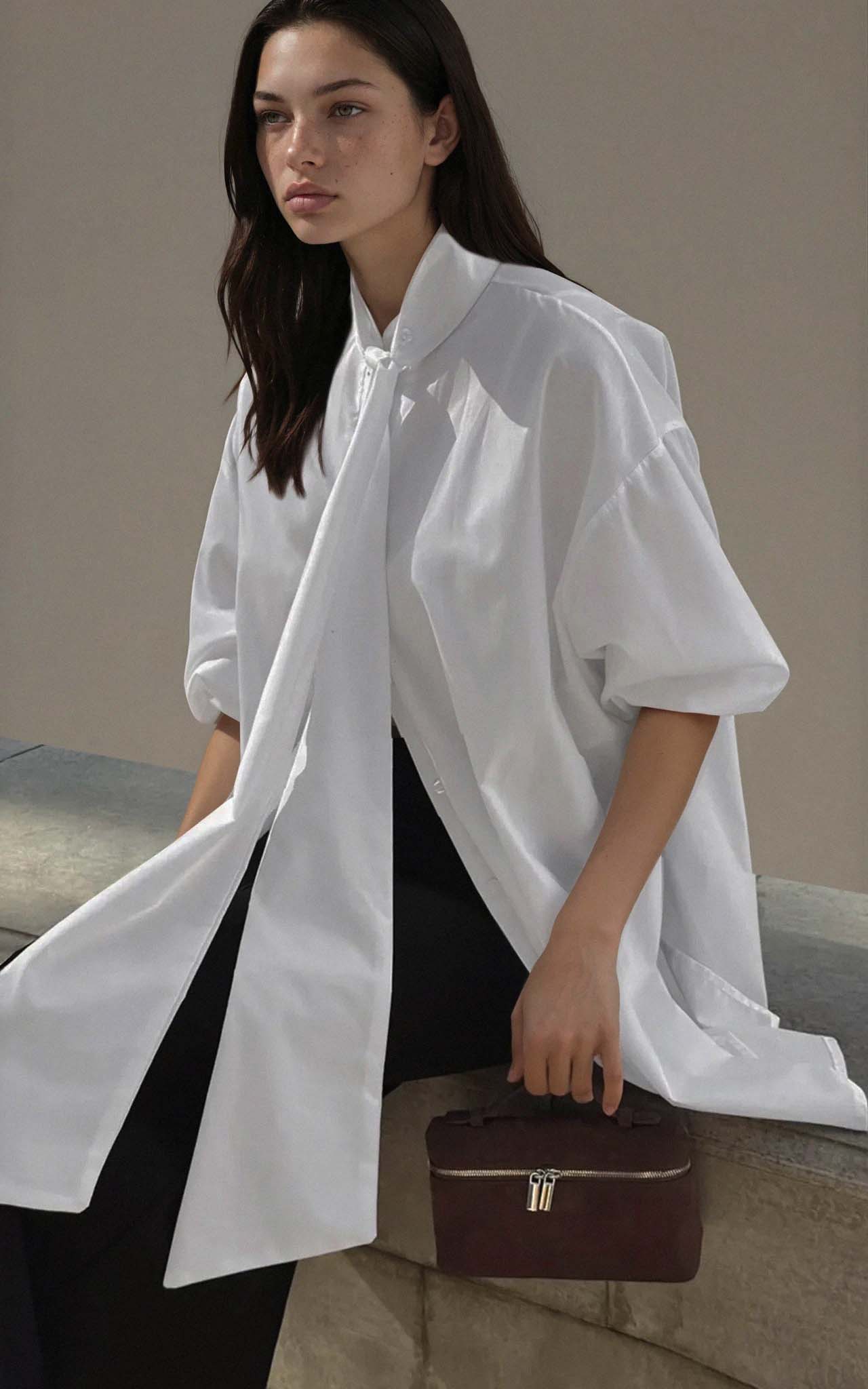 Woman wearing a white shirt holding a brown handbag against a neutral background