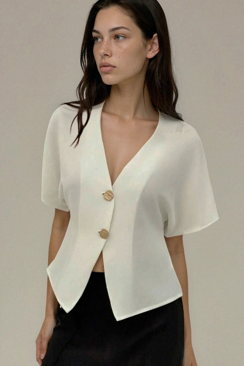 Woman wearing a white short-sleeve blazer over a black top against a neutral background