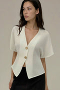 Woman wearing a white short-sleeve blazer over a black top against a neutral background