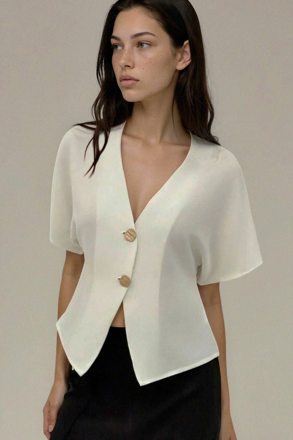 Woman wearing a white short-sleeve blazer over a black top against a neutral background