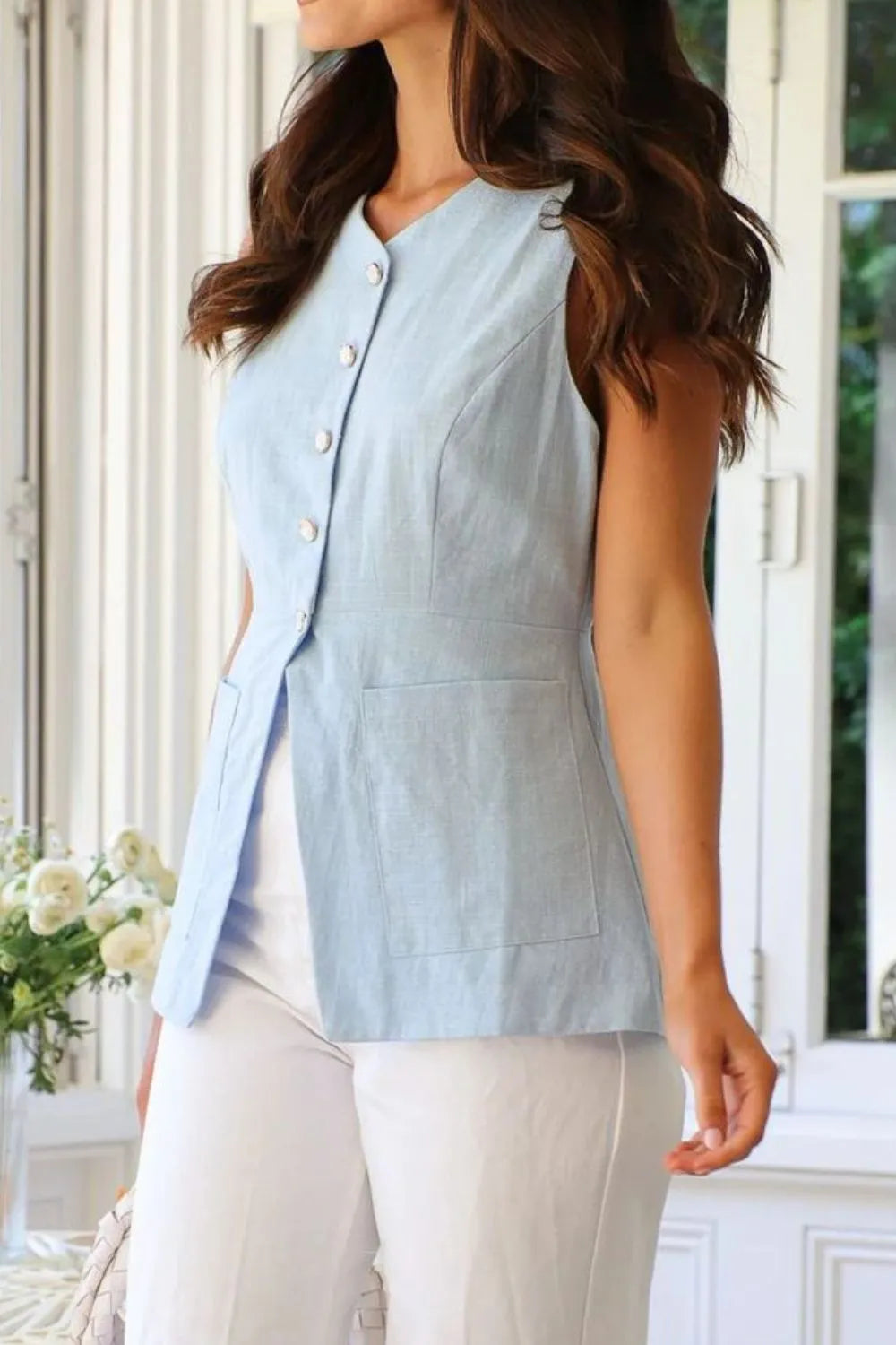 Woman wearing a light blue sleeveless vest in a bright room.