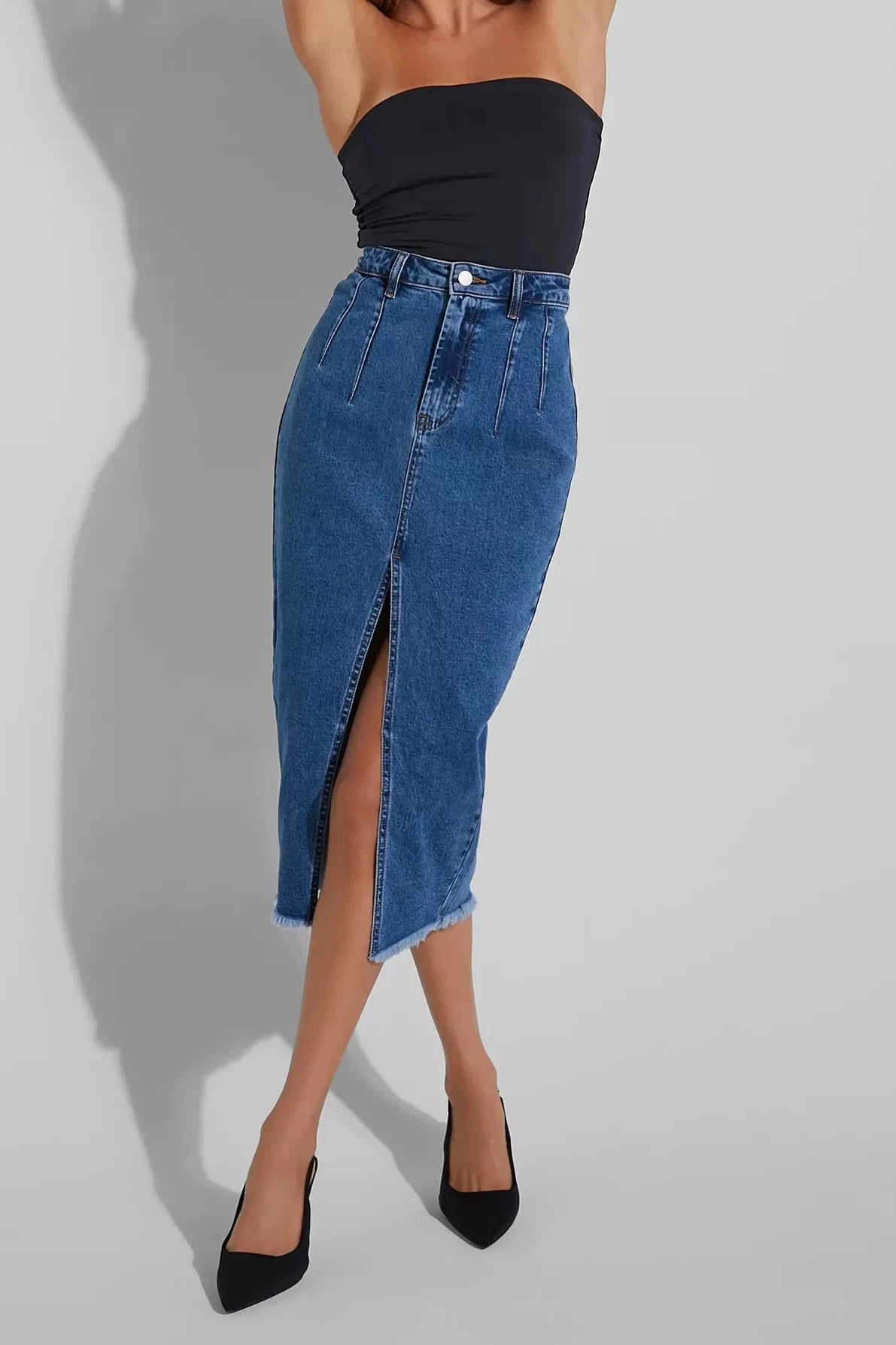 Person wearing a blue denim skirt with a slit on a gray background
