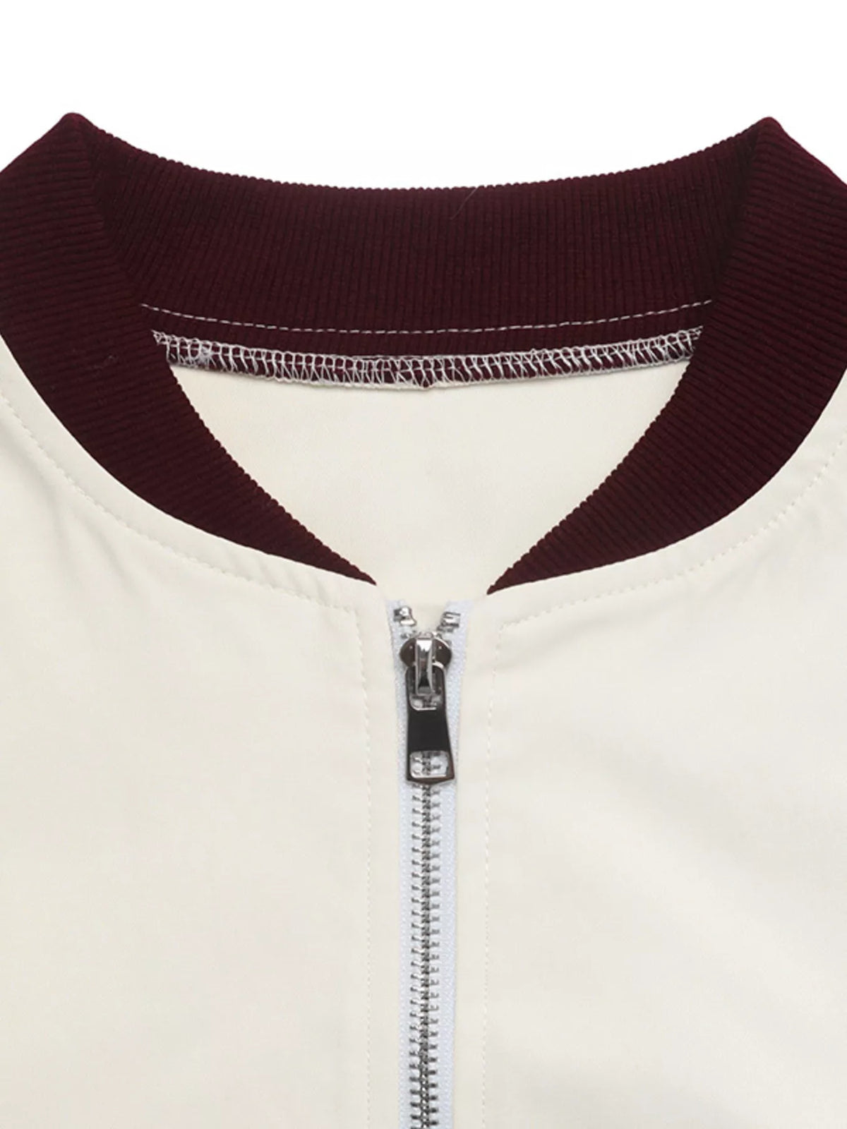 Close-up of a baseball-style jacket showing a cream-colored body and a contrasting dark burgundy ribbed collar, with a silver metal zipper.