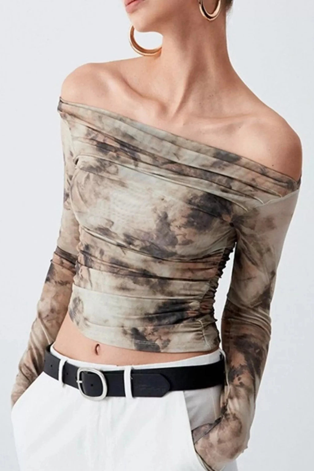 Woman wearing a long-sleeve, off-shoulder top with a tie-dye pattern on a plain background