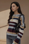 A woman wearing a fuzzy, long-sleeve striped sweater with navy, beige, and burgundy horizontal bands, paired with blue jeans and a black shoulder bag.