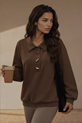 A woman wearing a brown long-sleeve knit sweater with a collar and decorative gold-toned buttons, holding a brown paper coffee cup against a warm beige background.