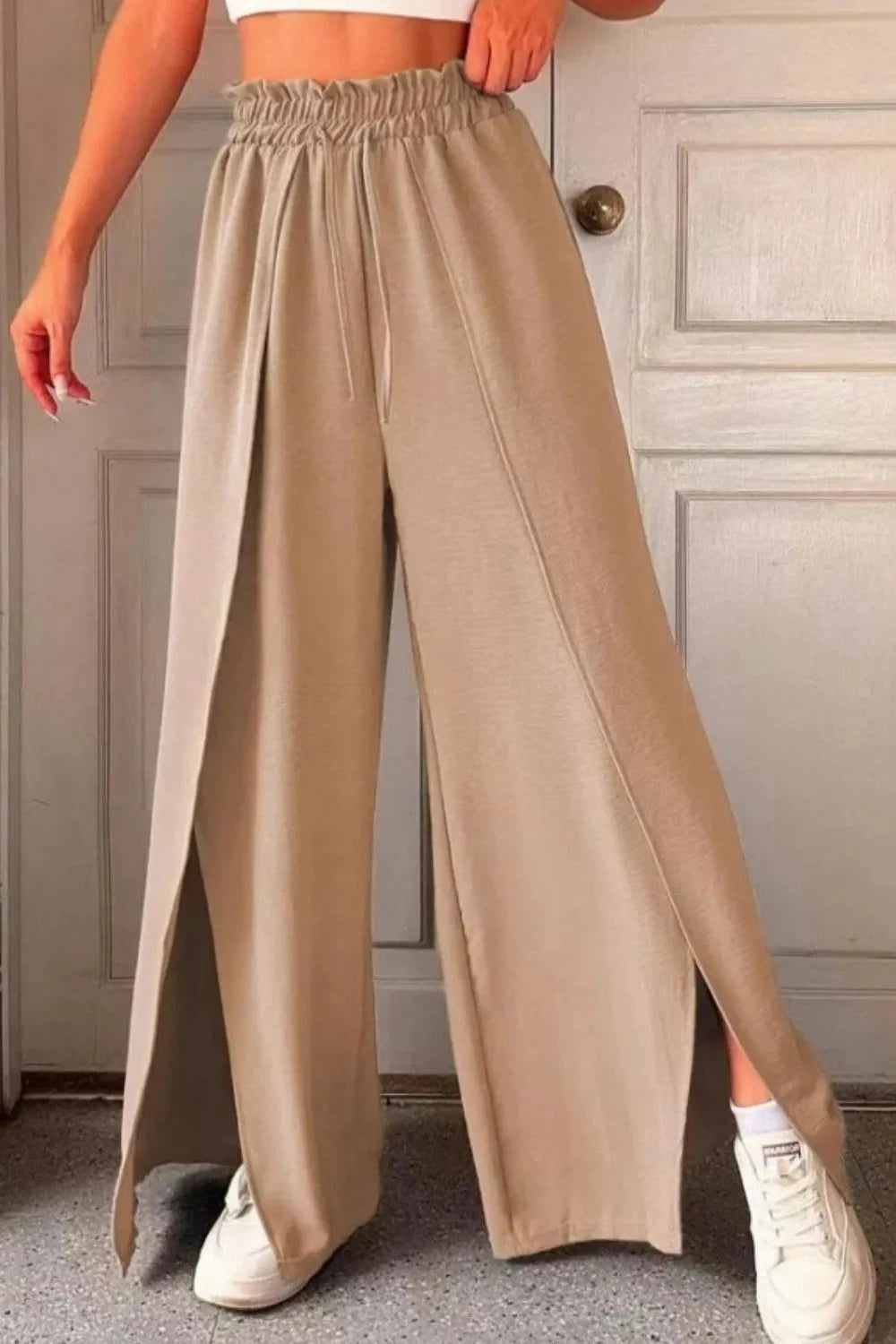 A pair of beige slit wide leg pants with a frill detail, displayed on a person.