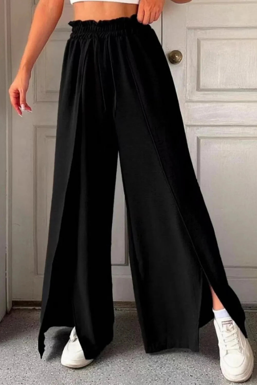 A pair of beige slit wide leg pants with a frill detail, displayed on a person.
